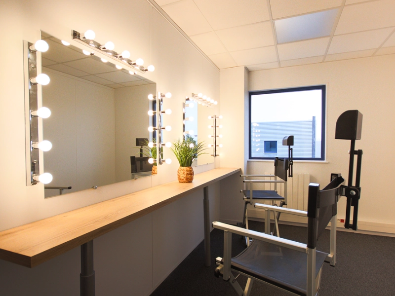 Loge de maquillage professionnelle entièrement équipée avec miroirs lumineux et chaises hautes pour la préparation avant tournage